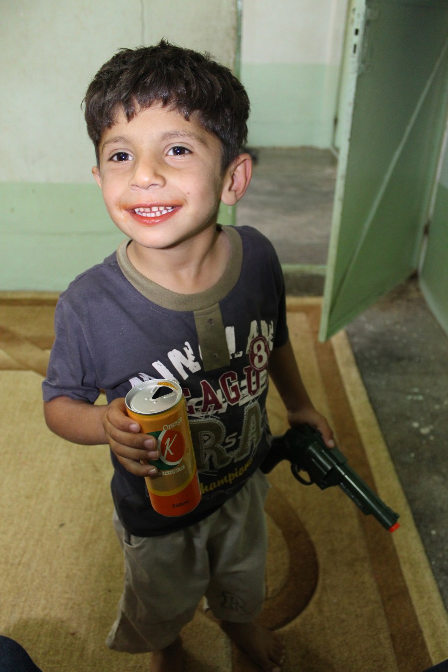 Oh, Hama is SUCH a Kurdish child. Mouth orange from a soda and holding a toy gun.